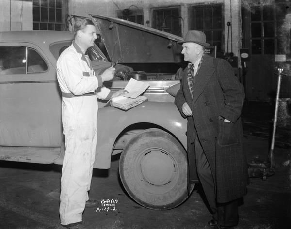 A mechanic discussing car repairs with a customer at the Schultz Tire and Battery Service, located at 1336 Regent Street.