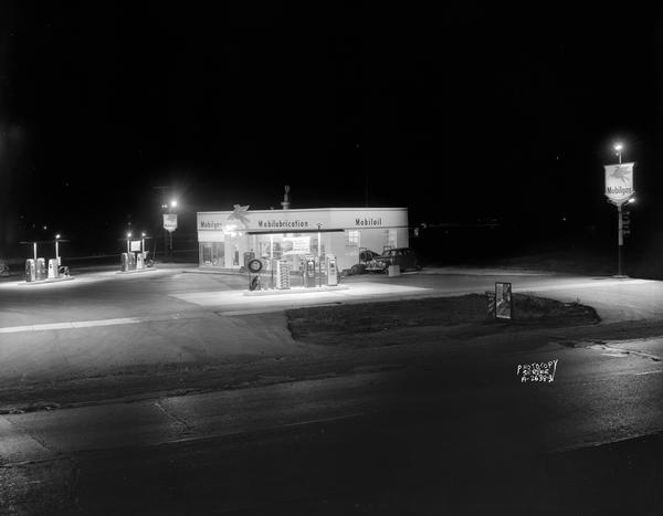 Night view of Mobil gas station at the corner of Highway 51 and East Washington including station, gas pumps, one automobile, and a "Mobilgas" sign on a pole.