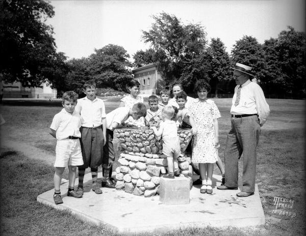 Children with Fred Winkelmann around the John L. Bourke drinking fountain, designed by Fred Winkelmann, Director of the Henry Vilas Zoo (Vilas Park Zoo). The fountain is located at the edge of the Vilas Park playground. Bourke was secretary of the Park and Pleasure Drive Association.