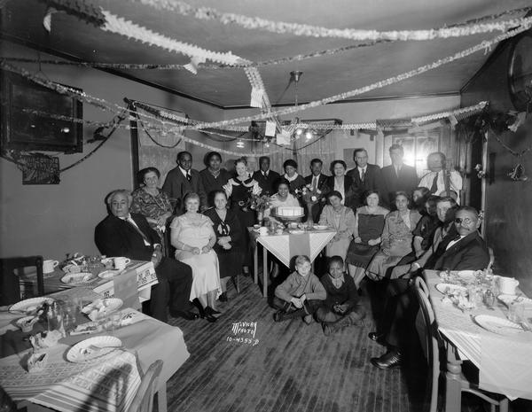 Beatrice Gulley's (Mrs. Carson Gulley) birthday party. Group portrait of family and friends posing around a small table with birthday cake and flowers.