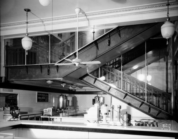 Glass enclosed stairway at F.W. Woolworth Company, located at 1 E. Main Street. There is a lunch counter underneath the stairs.