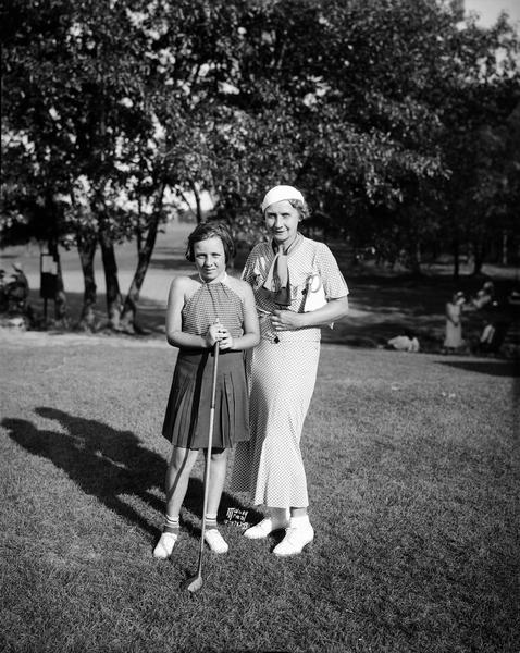 Portrait of Ruth Holt holding golf club, at the Nakoma golf course, age 10. She was the youngest player in the Junior Qualifying Round of the Wisconsin Women's Golf Association Tournament. Her mother, Emma Holt (Mrs. Edgar Holt), standing next to her, was the Association chairman.