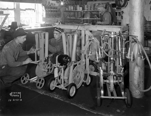 Three male workers testing the "Clean Easy Milker" milking machines at the Ben H. Anderson Mfg. Company, 3220 Atwood Avenue.