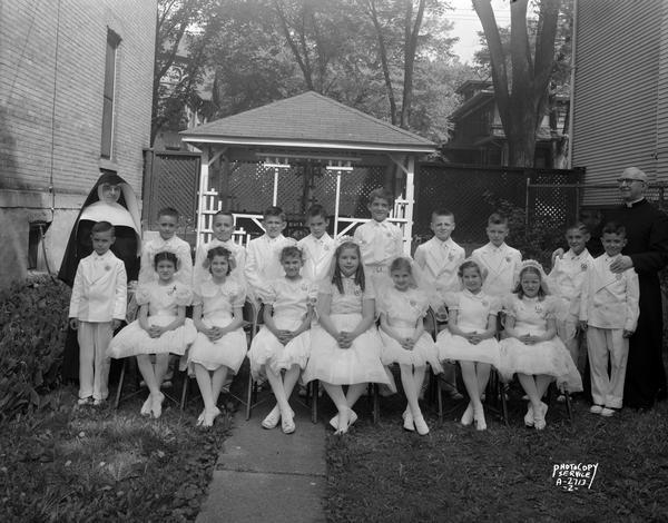 First communion group of 10 boys and seven girls with a priest and nun at Holy Redeemer Church, located at 128 West Johnson Street.