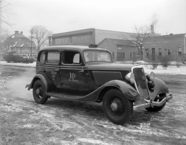 A Ford V-8 Yellow Cab Co. taxicab on East Washington Avenue. In the background are (left to right) St. Patrick's school, 630 East Washington Avenue; residence, 644 East Washington Avenue; Auto-Inn Restaurant (Diner), 646 East Washington Avenue, Wadhams Oil Co. Station, 648 East Washington Avenue; Blount Street; Pyramid Motor Company, 702 East Washington Avenue; and Central Fuel and Supply, 730 East Washington Avenue.