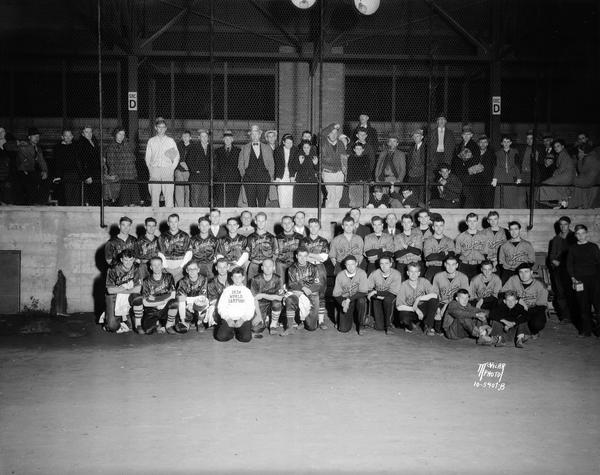 Bowman softball team in uniform and Kenosha Ke-Nash-As softball team in uniform. There are spectators in the bleachers behind the teams at Breese Stevens Field. Bowman won the state championship and qualified for a national tournament in Chicago.