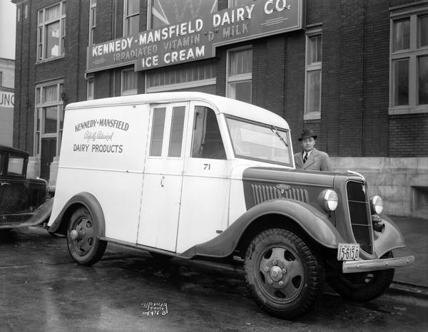 Kennedy-Mansfield Dairy truck parked in front of the Kennedy-Mansfield Dairy building, located at 621-629 West Washington Avenue. A man in a suit is standing behind the truck on the sidewalk.