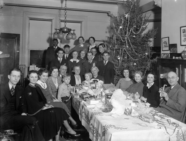 Group portrait of CUNA (Credit Union National Association) adults and children around a table with presents. There is a Christmas tree in the background.