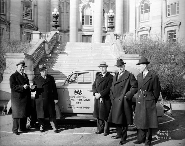 Governor Julius P. Heil and four men, standing next to a AAA dual control driver training car, courtesy of Pontiac Motor Division. The car is parked in front of the Wisconsin State Capitol steps.