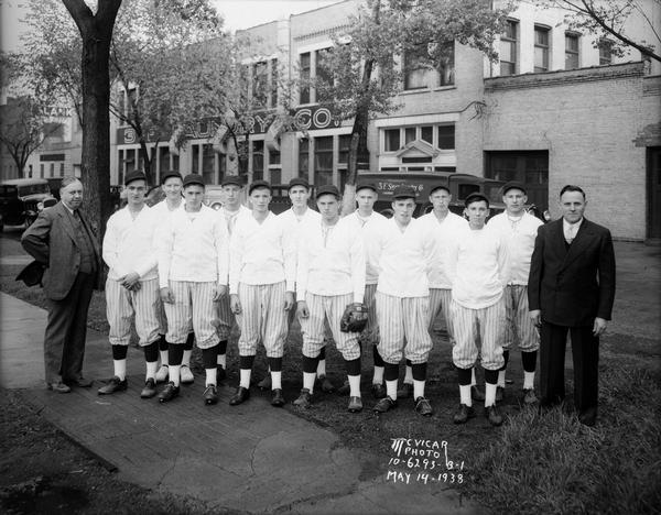 Outdoor group portrait of 3-F Laundry boys' baseball team, with 12 boys in uniform, and two men dressed in suits, in front of the 3-F Laundry plant, 731-747 East Dayton Street.