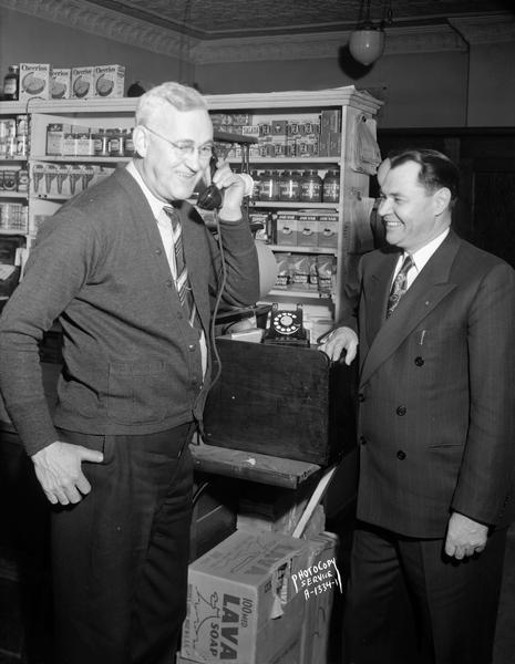 Charles T. Davies, Mazomanie representative of the Wisconsin Telephone Company, receives the first dial telephone call to be handled through the Wisconsin Telephone Company's new dial central office in Mazomanie, Wisconsin.  Mr. Davies receives the call at Davies & Son Store in Mazomanie, Wisconsin.  Witnessing the historic event is Truman Thompson, Mazomanie and Madison manager for the Wisconsin Telephone Company.  This telephone call was placed by Mazomanie Village President Theodore R. King.