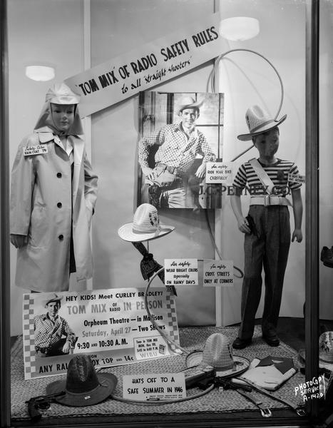 Display window at J.C. Penney & Company, 17-19 East Main Street, featuring cowboy "Tom Mix, of Radio, Safety Rules to All Straight Shooters" for Wisconsin Motor Vehicle Department Safety Division. Display features mannequin wearing "safety color raincoat at $3.98," a picture of Tom Mix "for safety ride your bike carefully." Another mannequin is wearing children's clothes and a cowboy hat "he helps prevent accidents." A pedestal holds a Tom Mix hat "wear bright colors especially on rainy days," and posters "for safety cross street only at corners and "Hey kids! Meet Curley Bradley, Tom Mix of radio, in person at the Orpheum Theatre." Also in the display are cowboy hats and ropes.