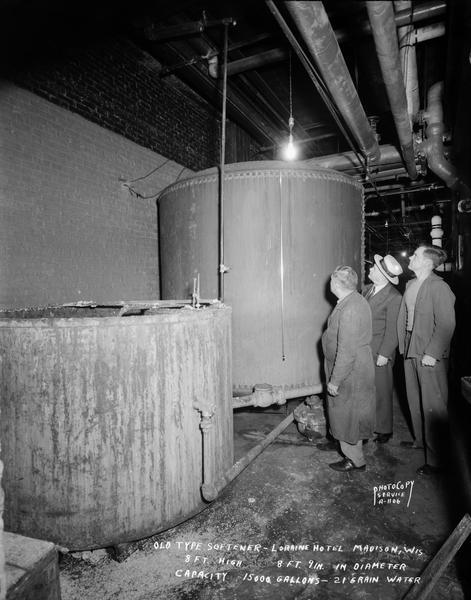 Three men look at an old style water softener in the basement of the Hotel Loraine, 123 West Washington Avenue. "Eight feet high, eight feet nine inches in diameter, capacity 1500 gallons - 21 grain water."
