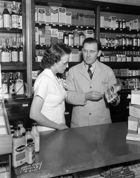 Rennebohm drugstore pharmacist showing a bottle of Pepto Bismol to a clerk.   