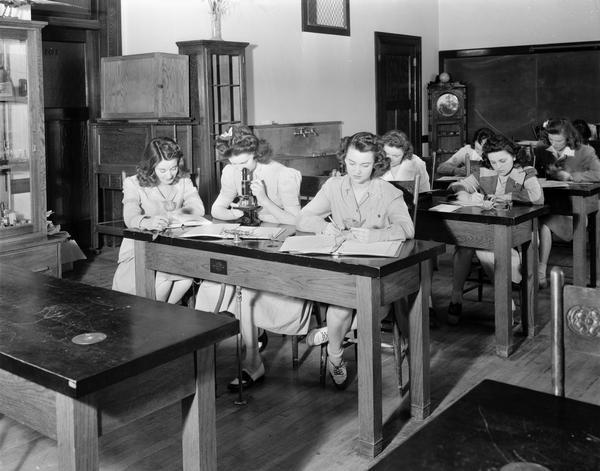 Seven Edgewood College (Sacred Heart Academy) women sitting at tables in Marshall Hall science laboratory, located at 1000 Edgewood Avenue.