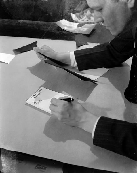 Close-up of a man writing a medical prescription for digitalis on a pad labeled: "John J. Doe, M.D. Brovira, Wis."