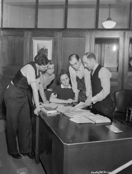 Five CUNA (Credit Union National Association) employees, four men standing and one woman sitting, around a desk at the new office, located at 1342 East Washington Avenue.