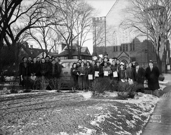 Group portrait of Central High School driving license class holding certificates and standing beside "AAA Dual Control Driver Training Car." They are standing in front of the First Methodist Church, located at 203 Wisconsin Avenue.
