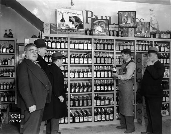 Five men (Saul Sinaiko and his son Donald Sinaiko and three others), standing in front of a liquor bottle display at the Badger Liquor Shop, 402 State Street.