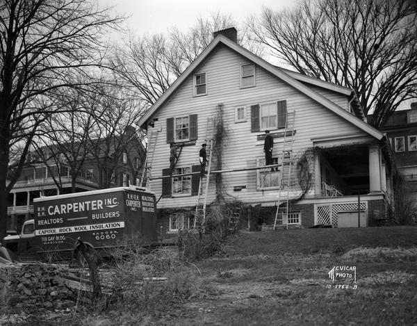 Three men on scaffolding are installing Capitol Rock Wool insulation, from a R.H. and E.H. Carpenter Inc. truck into a house at 616 N. Carroll Street.