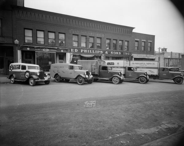 Five liquor delivery trucks parked in front of Ed Philips & Sons at 220-222 East Main Street in the Standard Fur Co. Building. Also shown in picture are Nelson Paint and Glass at 218 East Main street, Madison Armature and Parts at 224 East Main street and Epstein New Agency at 27 South Butler Street.
