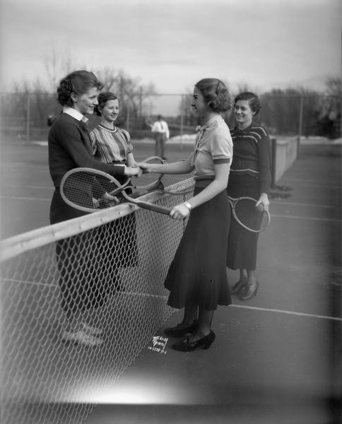 Four young women tennis players greeting each other at the net at Tenney Park's new tennis courts. From left to right are: Alta Mae Freund, Violette Spencer, Dorothy Peck and Helen Taubert.