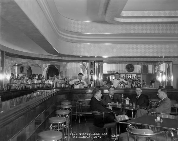 Interior of barroom at the Club Chanticleer, with two bartenders mixing drinks behind the bar, and four male patrons sitting at a table.