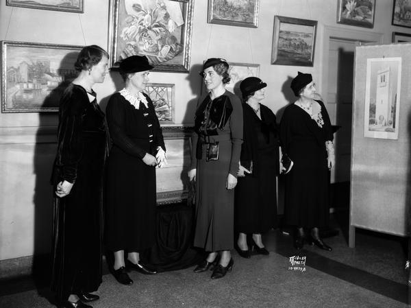 Portrait of five women viewing paintings of Madison artists exhibited at the Madison Women's Club, 240 W. Gilman Street. They include Hazel Jenks, president; Clara Piper, in charge of the exhibit; Beatrice Roberts, member of art committee; Nina Brinton and Lynne Lowman, in charge of the architectural exhibit.