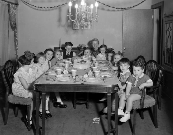 Eleven children and one adult are sitting around the table at Ronald Epstein's third birthday party.