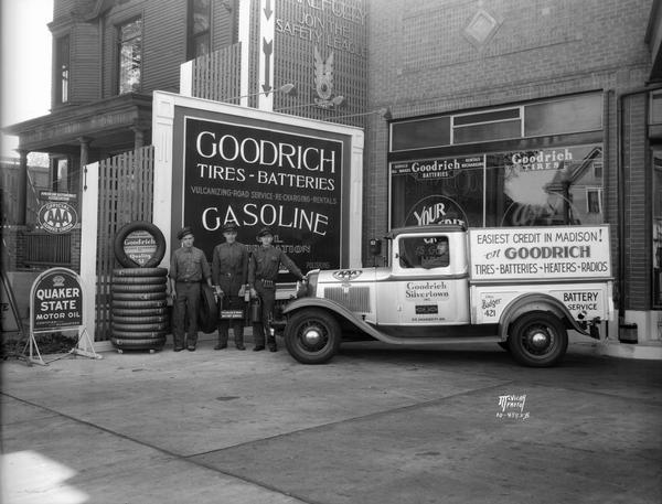 Three attendants are standing beside a Goodrich truck at Goodrich Silvertown, Inc. 515 University Avenue, next to a sign for Goodrich Tires and Batteries. A pile of tires is next to them.