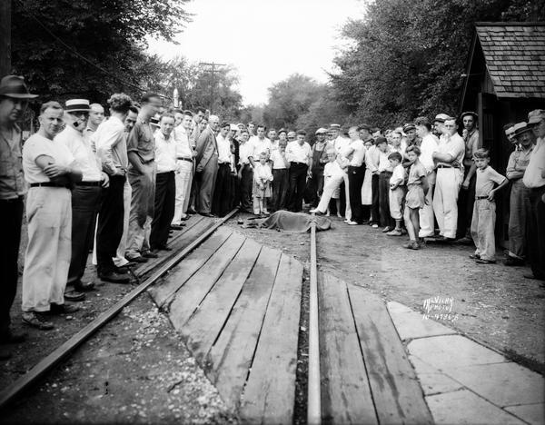 A large group of people stands around the covered body of H.C. Townley, Oregon school teacher, killed by a Milwaukee Road freight train, at the University Avenue crossing.