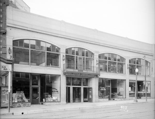 King Street facade of Arcade Building showing Madison Liquor store, 113 King; Capital City Bank, 111 King; Arcade Barbershop, 109 King; Charlier and Son jewelry company, 107 King; with Wisconsin State Employment Service upstairs and Constance Bennett in Moulin Rouge movie poster next to Majestic Theater.