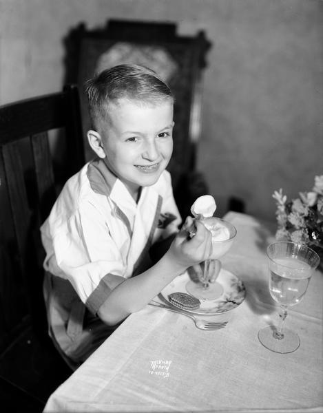 Richard McVicar is sitting at a table eating ice cream from a stemmed dish.