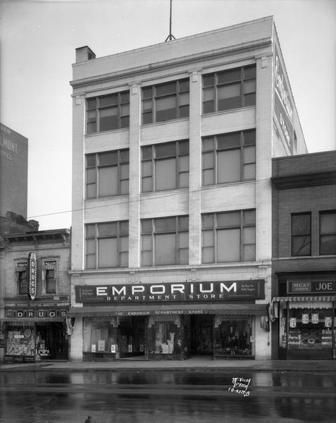 Emporium Department Store, 15-17 N. Pinckney, also showing Rennebohm Drug Store #6 on the left and Joe Tittle and Sons Meats on the right. The building occupied by the Rennebohm store was built about 1880. The modern metal facade which covered the building during the latter decades of the 20th century is now removed, revealing the somewhat altered original facade.