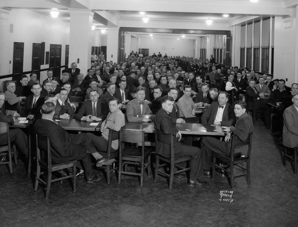 Large group of men sitting at tables playing in a Euchre tournament in Madison East High School cafeteria.
