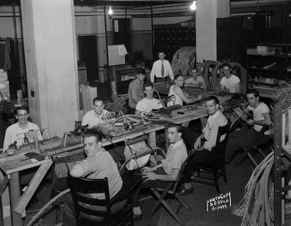 Eleven male workers and one supervisor making telephone switchboard cables in the basement of the Wisconsin Telephone Company building.