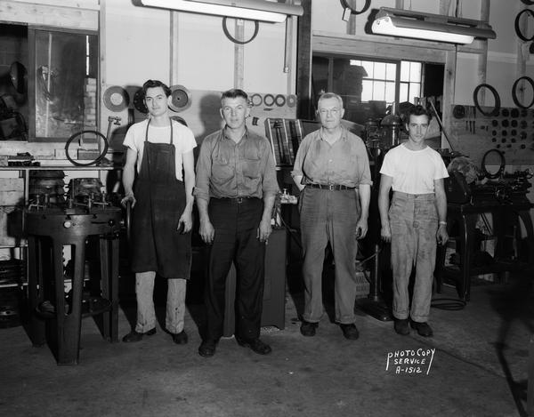 Winnebago Auto Parts Replacement Parts Company, 103 North Park Street. Four mechanics are standing in the shop in front of repair equipment.