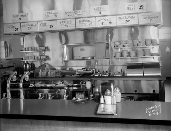 Interior of Kober's Dairy Bar drive-in restaurant, 2237 N. Sherman Avenue, showing the back bar with signs for menu items and prices.