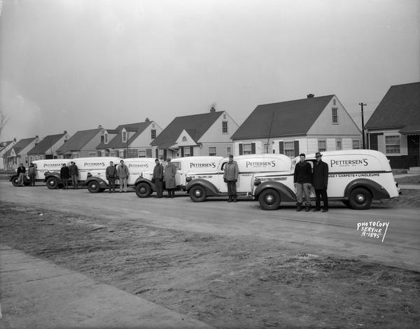 Line-up of six Pettersen's Inc., delivery trucks. Sign on trucks: "Rugs, Carpets, Linoleum." There are workmen standing next to trucks. Taken on the 2600 block of Myrtle Street.