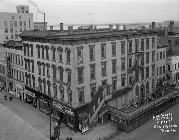Elevated view from the roof of the Park Hotel. Main Street businesses seen include, from the left: Western Union Telegraph Company at 21 West Main Street, Madison Bank and Trust Company at 23 West Main Street, Walk-Over Shoes at 25 West Main Street, Forbes-Meagher at 27 West Main Street, and Wisconsin Felton Sporting Goods at 29 West Main Street. A sign for the Wisconsin Engraving Company is attached to the building at the second floor level above the Wisconsin Felton Sporting Goods store. South Carroll Street businesses seen include: Charles Deans Barber at 103, Wisconsin Engraving Company at 109, Roick & Opsahl Lawyers at 111, and Master Blueprint Company at 113. Lake Monona is in the distance.