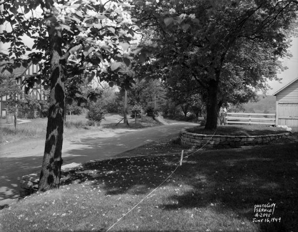 Freda Winterble property, 901 University Bay Drive, looking north toward Lake Mendota with a man holding a white rope across stone retaining walls, to show line for new road. Tudor house across the street, 902 University Bay Drive, was built by Robert A. Isom and sold to the First Unitarian Society for a parsonage. It was moved by the Society in 1963, when the road was widened, to 895 Cornell Court and is now their Annex.