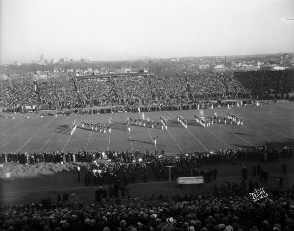 Minnesota marching band in formation spelling "MINN" at Camp Randall. The city skyline is in the background.
