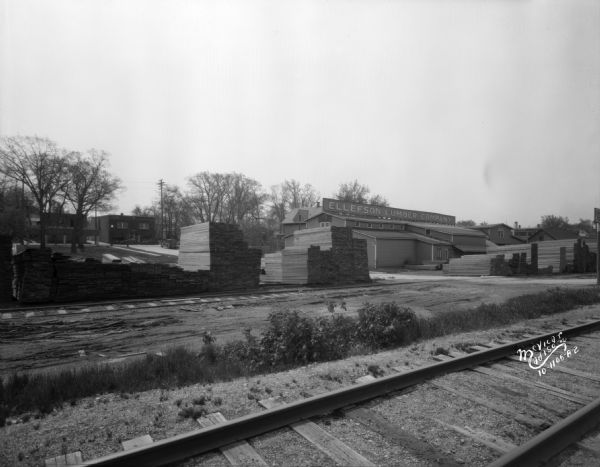 View across railroad tracks towards the Ellefson Lumber Company warehouse and yards on Sutherland Court behind 2016 Winnebago Street. 2039 Winnebago Street is in the background.