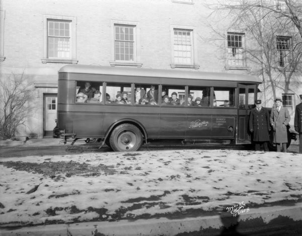 Disabled children in Hillington bus going to a free show at the Capitol Theatre. The bus driver and another man are standing beside the bus.