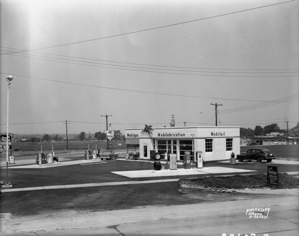 Daytime view of Robert Blossom's Mobil gas station, 3702 East Washington Avenue and Highway 51. In the background is the Club LaMark, and signs for Red Rooster Restaurant, Styleline Ornamental Iron, and The Idle House.