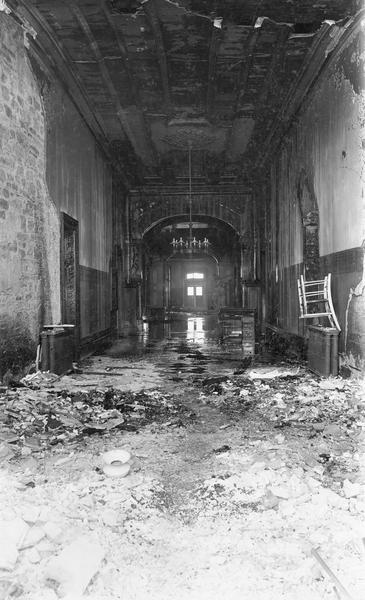 Damage caused to the third Wisconsin State Capitol by the fire of February 26-27. This photograph shows the first floor corridor, looking West. Still intact is a chandelier and its ceiling medallion.