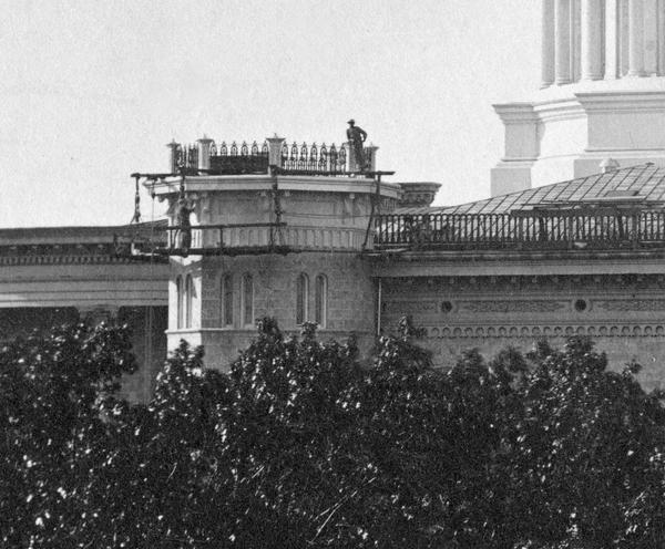 Painters working on the cornice of one of the four octagonal towers of the Wisconsin State Capitol. Also visible is the Italianate ornamentation of the iron cornice. Contemporary newspapers suggested that the iron cornice, columns, and dome required frequent painting, when their appearance became "rusty".