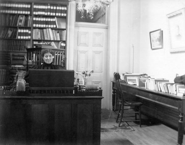 The office of Historical Society Librarian Minnie Oakley in the third Wisconsin State Capitol. From 1866 to 1883 the Historical Society occupied the entire second floor of the old South Wing. From 1883 to 1900 they occupied larger space in the South Wing addition. This photograph provides a close view of the panel doors and transom of the new wing and the office furniture.