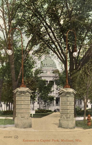 View of one of the four Prairie du Chien stone gateways that stood at the four corner entrances to the Capitol Park. More elaborate gates topped with iron statues stood at the center of each side of the park. The postcard also illustrates the electric lights that replaced the earlier gas lights. This postcard is postmarked 1909, indicating that depictions of the old Capitol continued to be sold even after the fire of 1904. The stone pillars remained in place until the present Capitol was completed (about 1917). The fire hydrant that was useless during the Capitol fire according to an ironic note. Caption reads: "Entrance to Capitol Park, Madison, Wis."