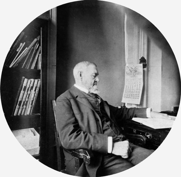 Daniel Steele Durrie, librarian of the Wisconsin Historical Society, seated at his desk in the South Wing of the Wisconsin State Capitol.  This photograph was taken by Reuben Gold Thwaites, secretary of the Historical Society, using a Kodak 2 camera format, a few months before Durrie's death. Durrie had been the librarian for 36 years, first under Lyman Draper and then under Thwaites.